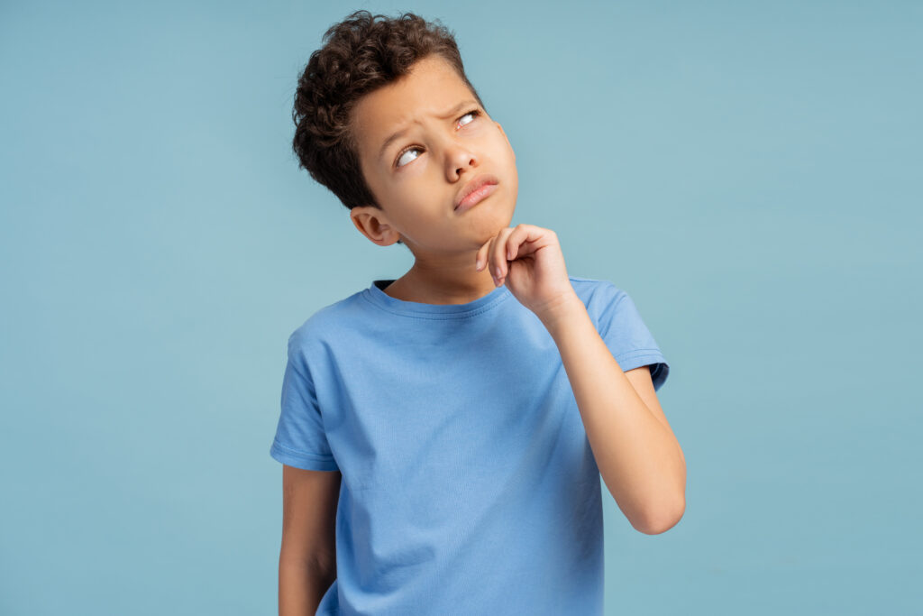 Boy thinking concentrated about doubt with finger on chin in studio isolated on blue background